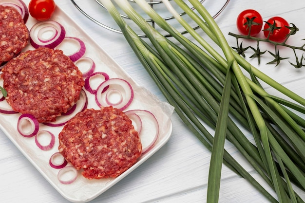 Zielona cebula i gałązka pomidora Surowe burgery wołowe z cebulą na talerzu