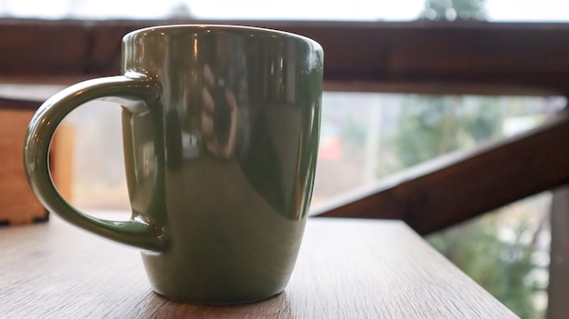 Zielona filiżanka z kawą lub herbatą na drewnianym stole na balkonie z widokiem na ulicę. Gorący napój na stole na werandzie letniej kawiarni. Nieostrość.