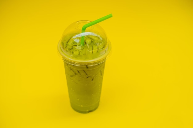 Zielona herbata latte z lodem w plastikowym kubku i słomka na żółtym tle Domowa mrożona Matcha Latte Herbata z mlekiem na wynos