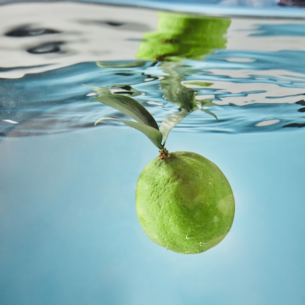 Zielona świeża limonka wpada do wody z falą nad powierzchnią wody. Koncepcja orzeźwiających letnich napojów
