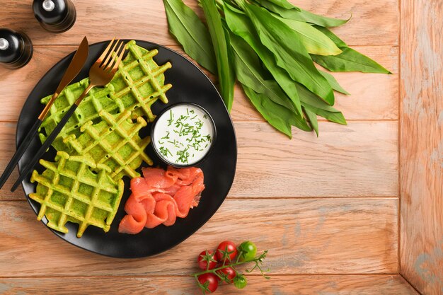 Zielone belgijskie gofry Gofry ze szpinakiem lub dzikim czosnkiem lub pesto z czerwonym łososiem i sosem śmietanowym na czarnym talerzu na ciemnym rustykalnym drewnianym tle Pyszna przekąska śniadaniowa brunch Widok z góry Makieta