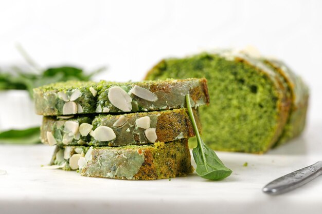 Zielone ciasto z płatkami migdałowymi pokrojonymi na marmurowej desce Kawałki Biszkoptowego zielonego ciasta ze szpinakiem