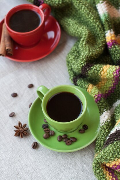 Zielone i czerwone filiżanki kawy z ziarnami kawy, gwiazdką anyżu i pałeczkami cynamonu