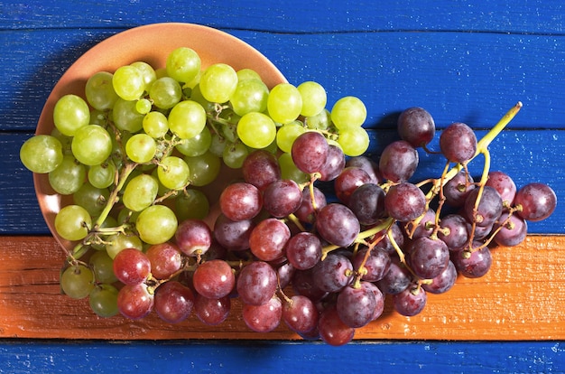 Zielone i czerwone winogrona w talerzu na kolorowym drewnianym stole, widok z góry
