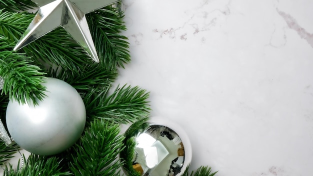 Zielone liście sosny na białym marmurowym tle, ozdoby świąteczne w jasnym srebrnym kolorze. Prosty i kreatywny pomysł na Boże Narodzenie.