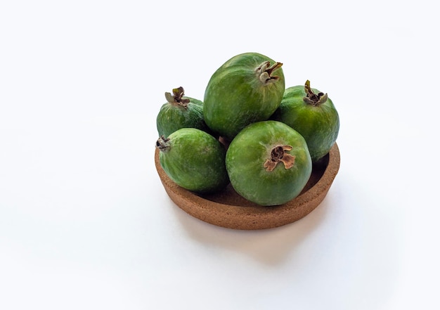 Zielone owoce feijoa w korkowym talerzu na białym tle