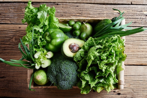 Zielone warzywa i owoce i zielenie w brązowym wiklinowym koszu na drewnianym tle. Koncepcja zdrowego odżywiania