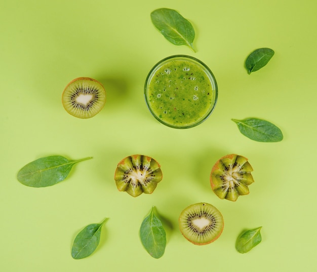 Zdjęcie zielony jarski smoothie na zielonym tle z kiwi połówkami i szpinakiem opuszcza, czysty łasowania pojęcie, odgórny widok