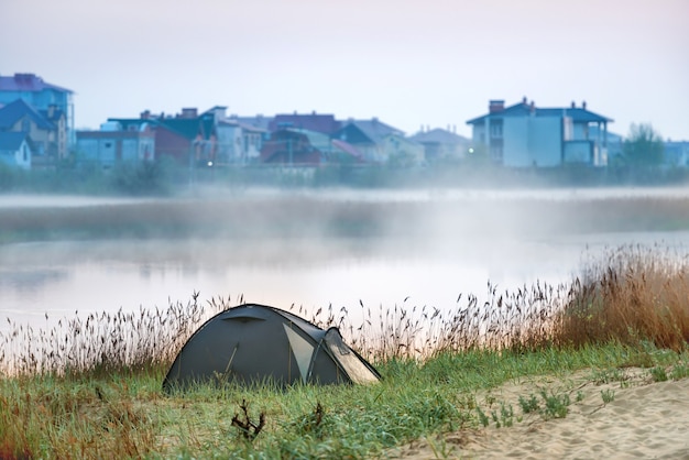 Zielony namiot w pobliżu rzeki z poranną mgłą na wodzie. Krajobraz podróży na świeżym powietrzu