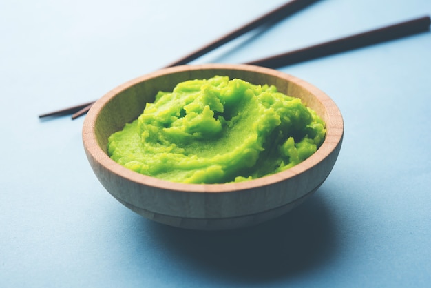 Zielony sos lub pasta wasabi w misce, pałeczkami lub łyżką na prostym kolorowym tle. selektywne skupienie