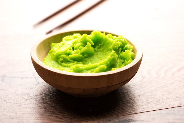 Zielony sos lub pasta wasabi w misce, pałeczkami lub łyżką na prostym kolorowym tle. selektywne skupienie