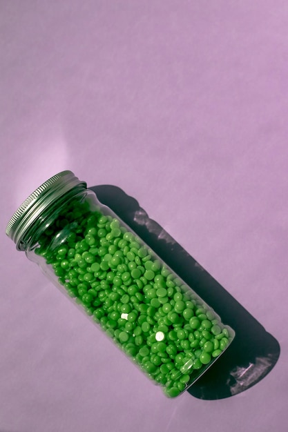 Zdjęcie zielony wosk do depilacji w granulkach na fioletowym tle słoik z woskiem na izolowanym tle