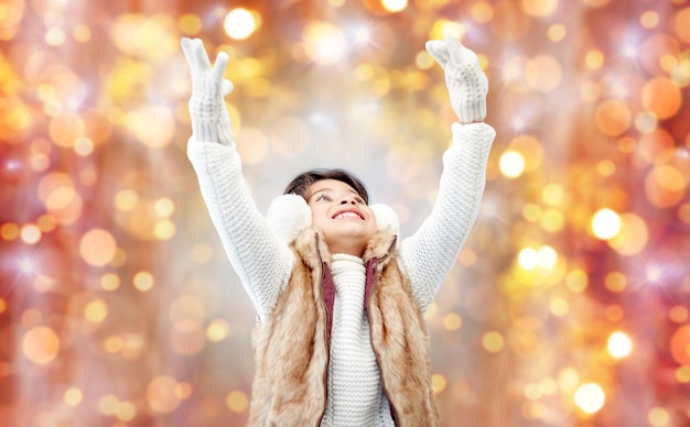 zima, ludzie, święta i koncepcja szczęścia - szczęśliwa mała dziewczynka w nausznikach i rękawiczkach na tle świateł świątecznych