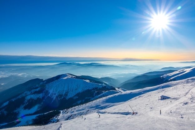 Zima na Słowacji. Ośrodek narciarski Jasna. Widok ze szczytu ośnieżonych gór na stok narciarski z narciarzami