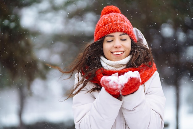 Zima uśmiechnięta kobieta w czerwonym kapeluszu pozuje w zaśnieżonym parku Zimna pogoda Zimowe wakacje w modzie