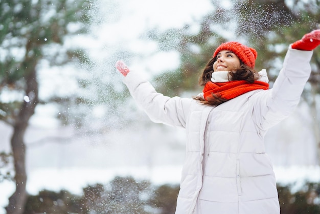 Zima uśmiechnięta kobieta w czerwonym kapeluszu pozuje w zaśnieżonym parku Zimna pogoda Zimowe wakacje w modzie