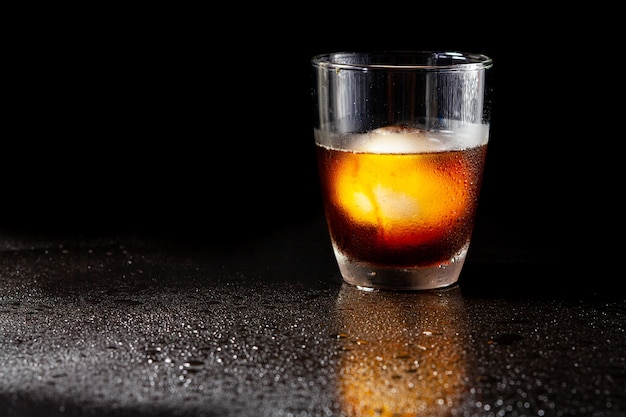 Zimna dekoracja americano z kulką lodu w szklance whisky na czarnym stole.