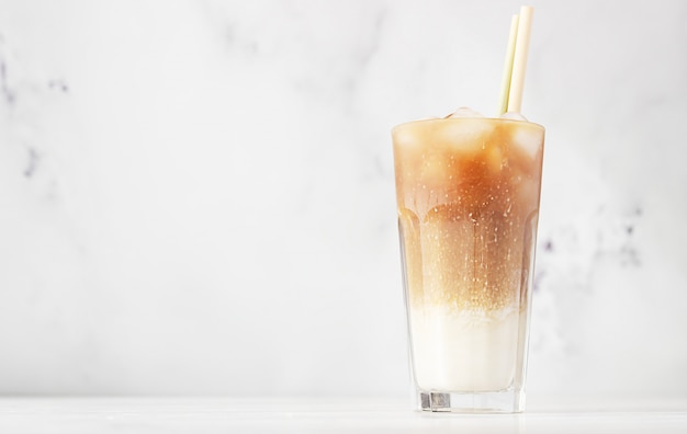 Zimna kawa z mlekiem i kostkami lodu w wysokiej szklance ze słomką bambusową