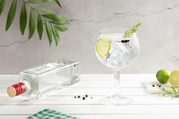 Zdjęcie zimna szklanka ginu z tonikiem i butelka na białej drewnianej podstawie na jasnym tle