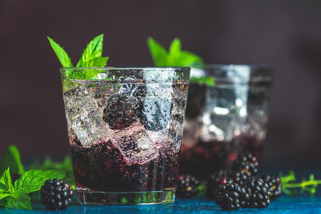 Zimny letni napój jagodowy z jeżynami Orzeźwiający letni napój z syropem jeżynowym i lodem na ciemnoniebieskim betonowym tle