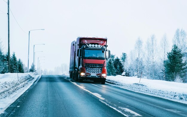 Zdjęcie zimowa droga ze śniegiem. ciężarówka w finlandii. samochód ciężarowy i zimny krajobraz laponii. las europy. jazda autostradą po fińskim mieście. drogą i trasą zaśnieżoną ulicę. dostawa w jeździe zjazdowej