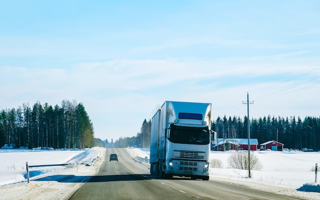 Zimowa droga ze śniegiem. Ciężarówka w Finlandii. Samochód ciężarowy i zimny krajobraz Laponii. Las Europy. Jazda autostradą po fińskim mieście. Drogą i trasą zaśnieżoną ulicę. Dostawa w jeździe zjazdowej