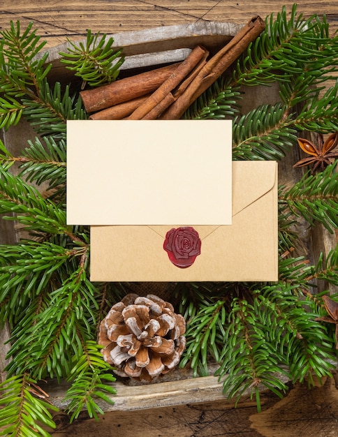 Zimowa kompozycja bożonarodzeniowa z pustą kartą i zapieczętowaną kopertą na drewnianym stole. Boże Narodzenie i nowy rok szablon karty z pozdrowieniami z gałęzi jodły i szyszki sosnowe widok z góry. Wakacyjna makieta