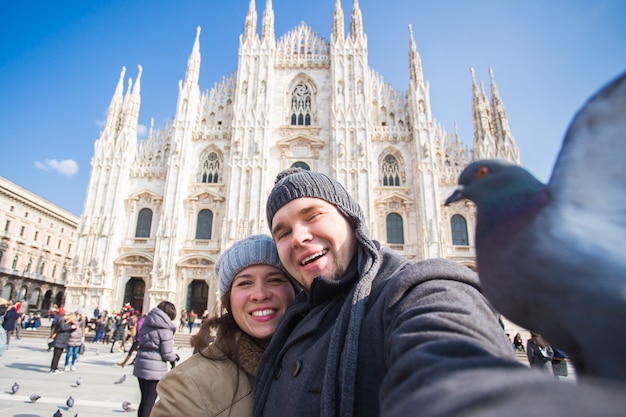 Zimowa Koncepcja Podróży I Wakacji - Szczęśliwi Turyści Robiący Autoportret Ze śmiesznymi Gołębiami Przed Katedrą Duomo W Mediolanie