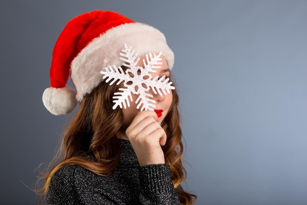 Zimowa koncepcja szczęścia ludzi Kobieta w świątecznym kapeluszu zamyka twarz dużym srebrnym płatkiem śniegu