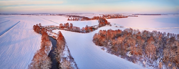 Zimowa panorama Pokryte śniegiem pola łąki Rzeka zamarznięte drzewa wieś w wieczornym świetle Wiejski krajobraz zachodzącego słońca Polna droga w lodzie Widok z lotu ptaka