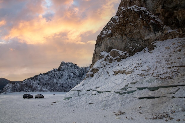 Zimowa podróż samochodem Zimowy krajobraz góry i skały pokryte lasem na brzegu zamarzniętej rzeki na tle zachodzącego słońca nieba