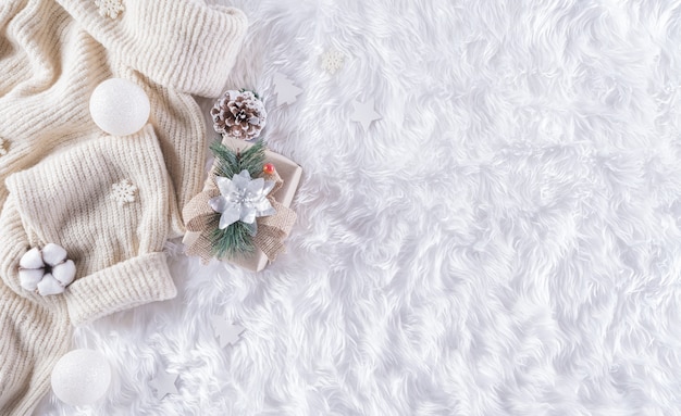 Zimowa przytulna ściana z filiżanką kawy, ciepłym swetrem, pudełkiem prezentowym, kwiatem bawełny i bombką na wełnianej ścianie dywanowej, widok z góry z miejscem na kopię.