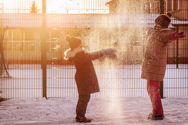 Zimowe dzieci bawiące się śniegiem w Snowy Yard. Szczęśliwe dzieci bawią się rzucając śniegiem. Światło słoneczne.