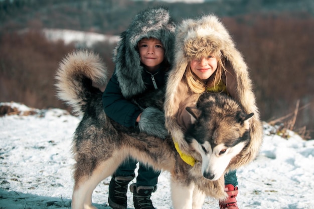 Zimowe dzieci przytulają husky w śniegu w zimowym lesie