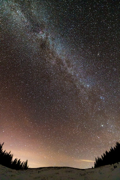 Zimowe góry nocy krajobraz panorama. Jasna konstelacja Drogi Mlecznej na ciemnoniebieskim gwiaździstym niebie