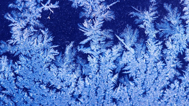 Zimowe mroźne okno. Niebieskie tło szronu, kryształki lodu na szkle