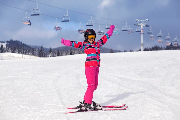 Zimowe narty w górach. Szczęśliwa dziewczyna dziecko na nartach, ciesząc się śniegiem na tle wyciągu narciarskiego.