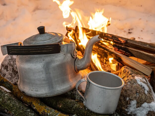 Zimowy kemping ze stalowym czajnikiem i żywym ogniem w śnieżnej scenerii