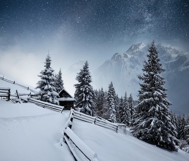 Zdjęcie zimowy krajobraz. górska wioska w ukraińskich karpatach. wibrujące nocne niebo z gwiazdami, mgławicą i galaktyką. astrofotografia głębokiego nieba.