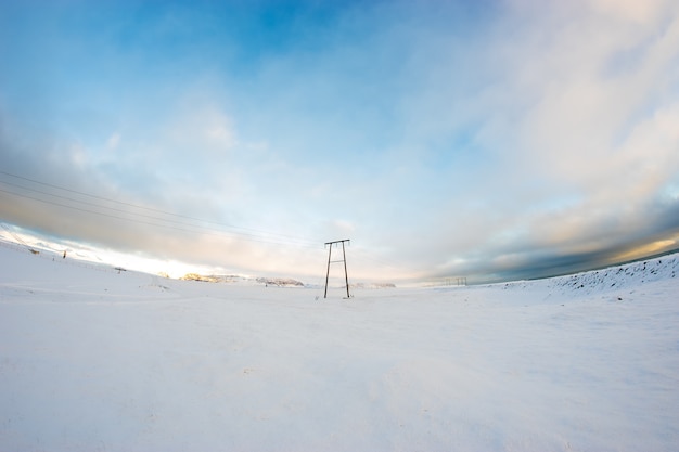 Zimowy krajobraz, linie energetyczne na zaśnieżonym polu pod górami, Islandia