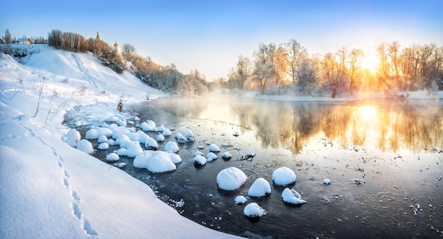 Zimowy krajobraz nad rzeką to wczesny słoneczny mroźny poranek i śnieżne kępy w wodzie