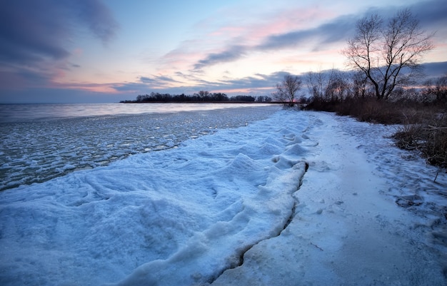 Zimowy krajobraz z zamarzniętym jeziorem i zachodem słońca niebo. Kompozycja natury.