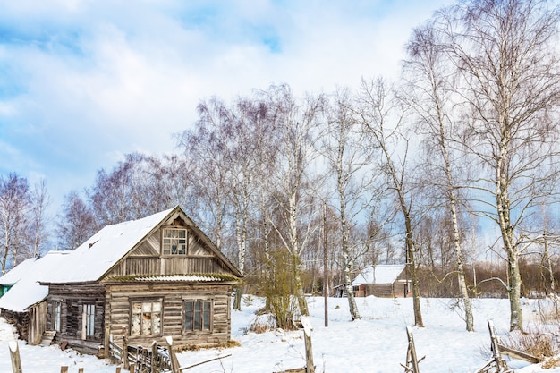 Zimowy krajobraz ze starym drewnianym domem i drzewami z niebieskim pochmurnym niebem,