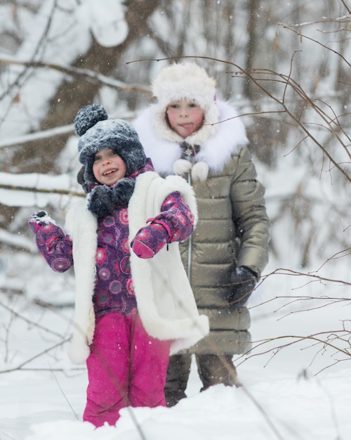 Zimowy las dwie małe dziewczynki bawiące się śnieżkami uśmiechnięte