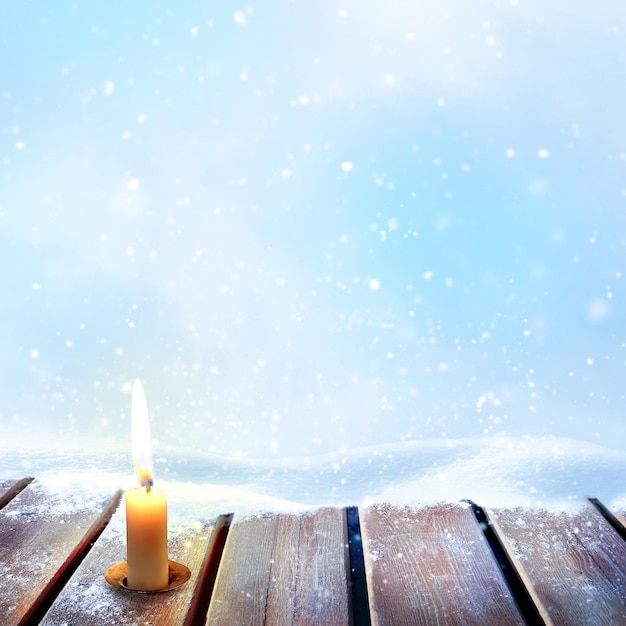 Zimowy obraz bożonarodzeniowy Świeca na drewnianej powierzchni na tle zasp i opadów śniegu Kwadratowy obraz Kopiowanie miejsca