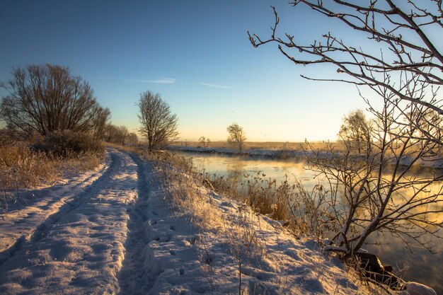 Zimowy pejzaż ze śniegiem, rzeką, niebieskim niebem, drogą, światłem słonecznym, lodem.