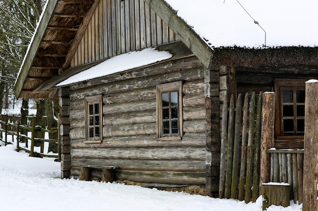 Zimowy rosyjski krajobraz Stara drewniana chata Dom z bali z dachem krytym strzechą Opuszczona rosyjska wieś pokryta śniegiem Dom z bali ze stodołą
