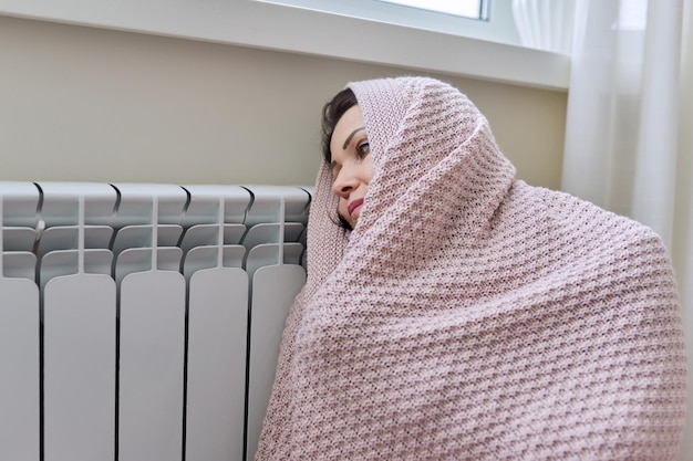 Zimowy sezon grzewczy Kobieta w ciepłym swetrze siedzi w pokoju domowym w pobliżu grzejnika
