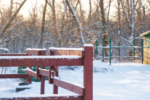 Zimowy wiejski krajobraz, w tle zaśnieżony las, na pierwszym planie czerwony drewniany płot