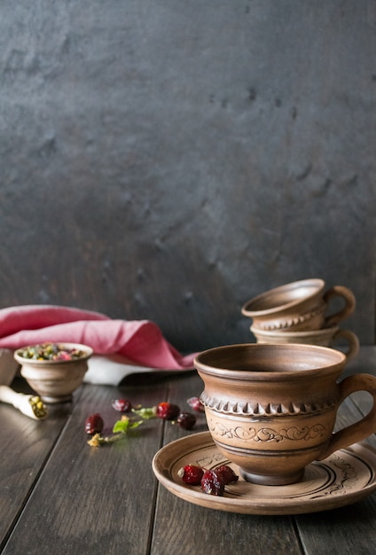 Ziołowa herbata, ziele i kwiaty w glinianej filiżance na drewnianym stole